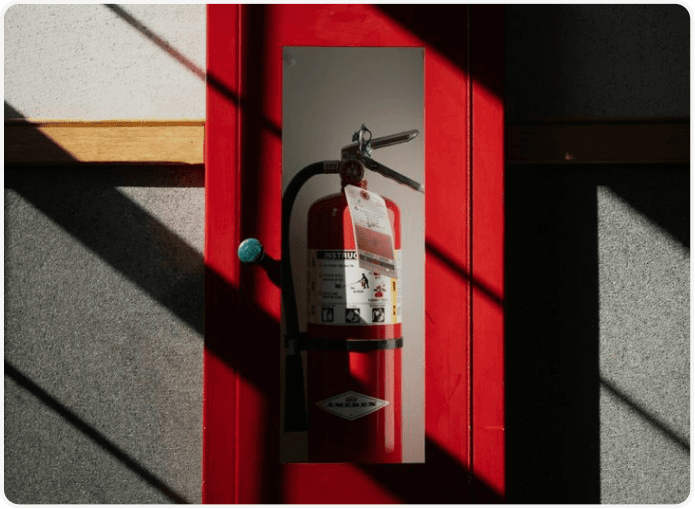 Fire extinguisher inside a red doorway with dramatic shadows