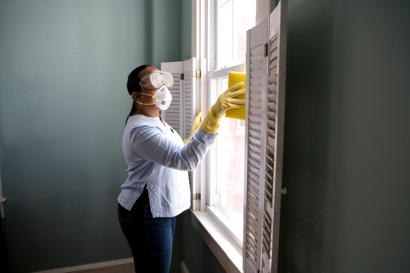 Technician in protective gear spraying along a baseboard indoors